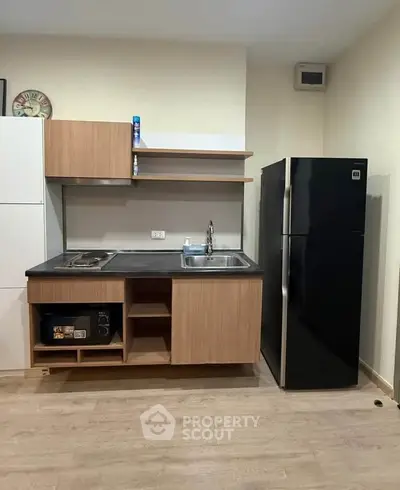 Modern compact kitchen with sleek black fridge and wooden cabinetry.