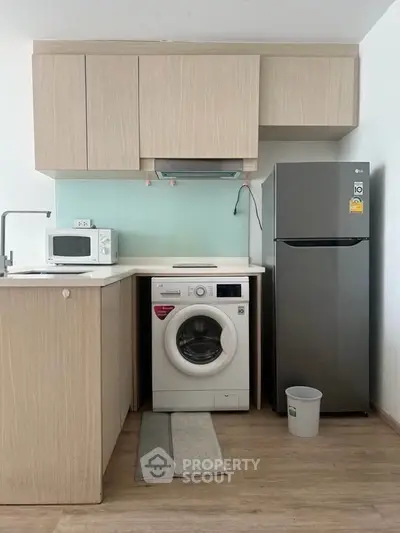 Modern kitchen with washing machine, fridge, and microwave in compact layout.