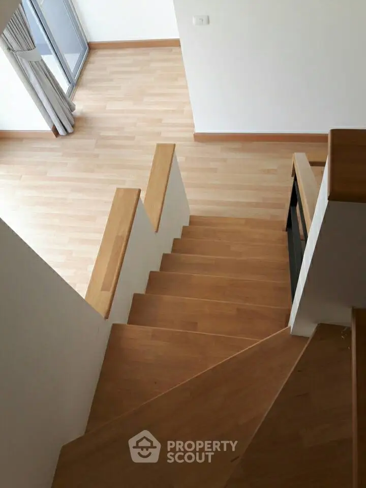 Modern wooden staircase leading to a bright open living area with large windows.