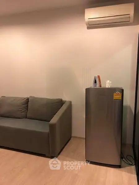 Modern living room with sleek sofa and compact fridge under air conditioning unit.