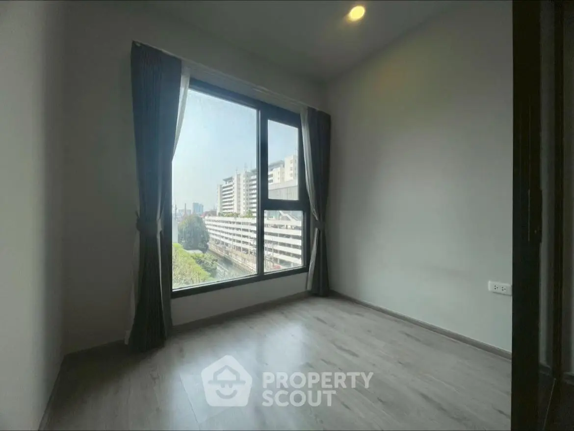 Spacious bedroom with large window offering city view and natural light.