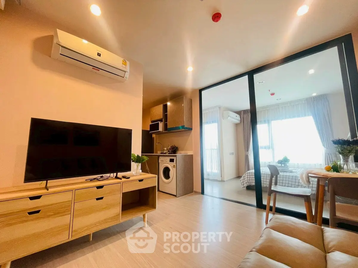 Modern open-plan living room with TV, washing machine, and bedroom view.