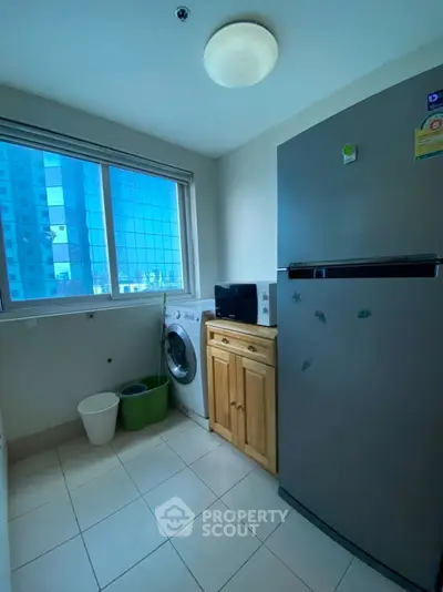 Bright utility room with washing machine, fridge, and city view window.