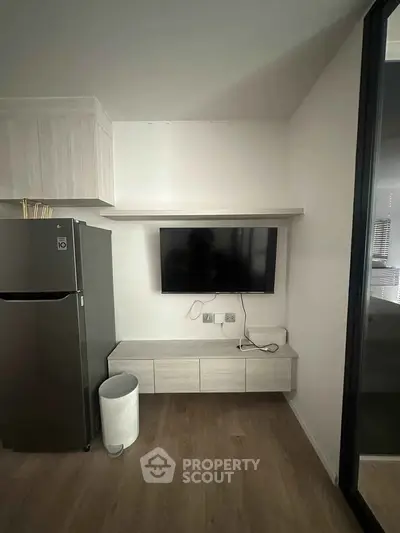Modern kitchen with sleek cabinetry, wall-mounted TV, and stainless steel fridge in a stylish apartment.