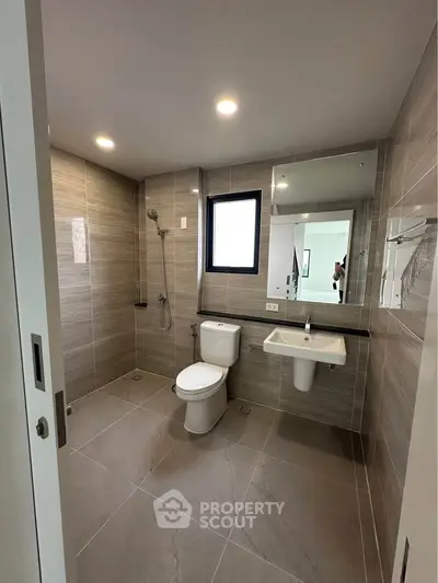 Modern bathroom with sleek fixtures and large tiles, featuring a shower and toilet.