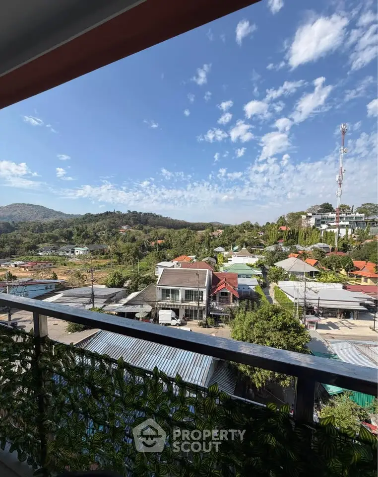 Scenic balcony view overlooking lush hills and residential area under a clear blue sky.