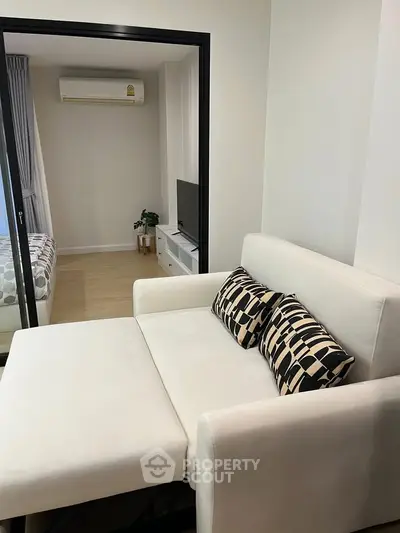 Modern living room with stylish sofa and view into cozy bedroom