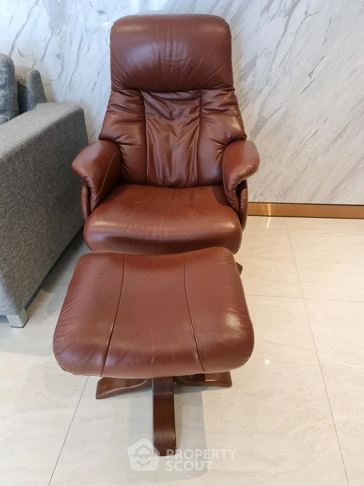 Luxurious brown leather armchair with matching footrest on elegant marble flooring, perfect for modern living room.