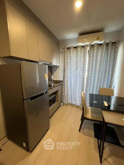 Modern kitchen with sleek cabinetry, dining area, and large fridge in cozy apartment setting.
