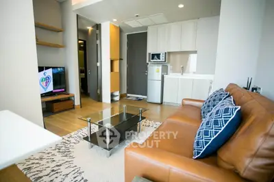 Modern living room with leather sofa, glass coffee table, and open kitchen layout.