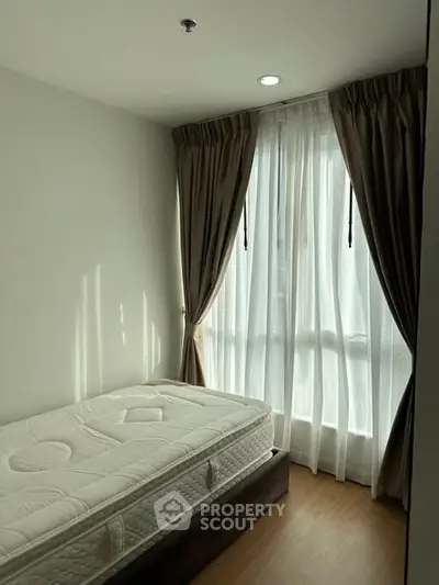 Cozy bedroom with natural light and elegant curtains, featuring a comfortable mattress.