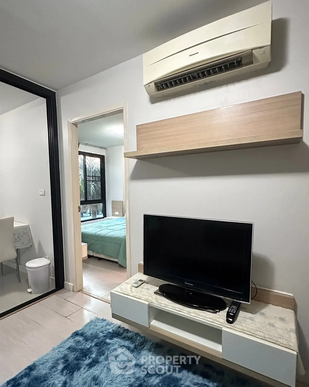 Cozy living room with modern TV setup and air conditioning, adjacent to a stylish bedroom.