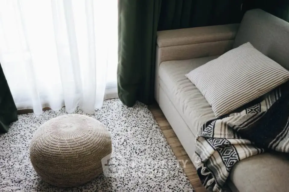 Cozy living room with stylish sofa, textured rug, and natural light through large windows.