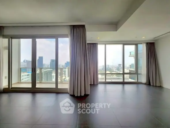 Spacious modern living room with floor-to-ceiling windows offering stunning city views in a high-rise apartment.