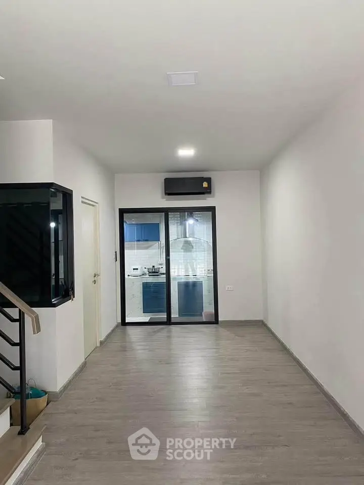 Spacious modern living area with sleek flooring and view into a stylish kitchen.