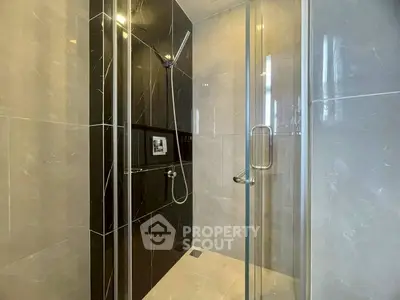 Modern bathroom with sleek black and gray tiles and glass shower enclosure.
