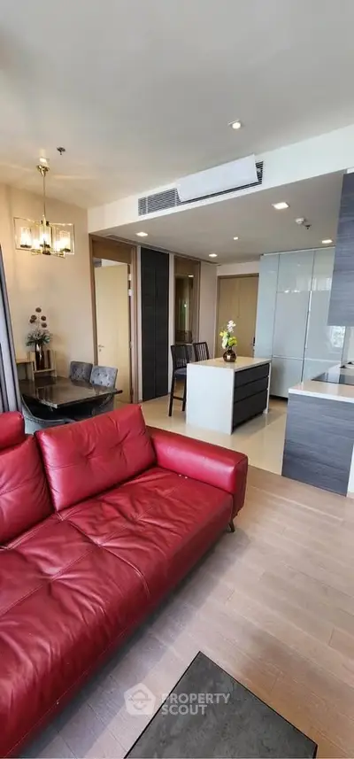 Modern living room with red leather sofa and open kitchen layout in a stylish apartment.