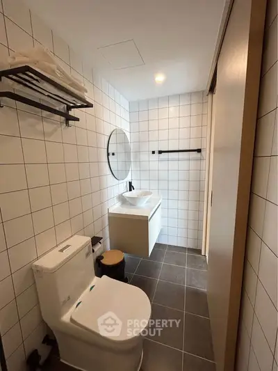 Modern bathroom with sleek design and tiled walls, featuring a toilet and vanity.
