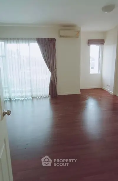 Spacious empty room with wooden flooring and large windows for natural light.