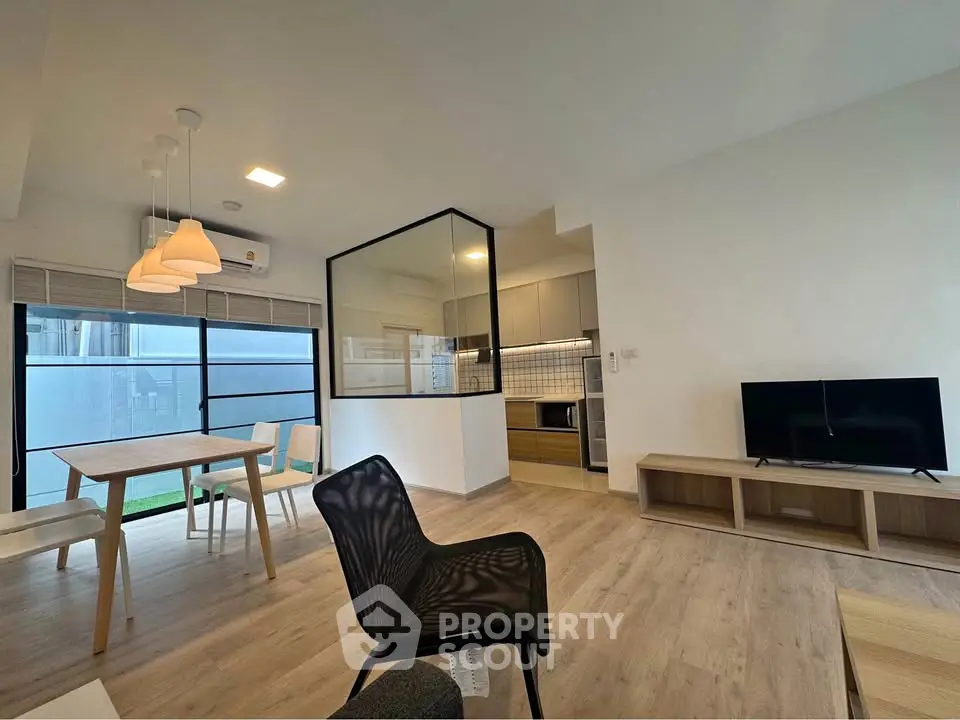 Modern open-plan living room with stylish kitchen and dining area, featuring sleek furniture and natural light.