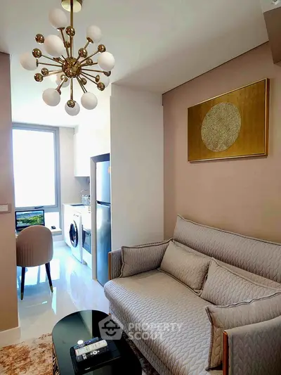 Modern living room with elegant chandelier and cozy sofa, adjacent to a compact kitchen with washing machine.