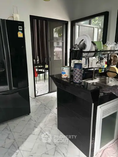 Modern kitchen with sleek black appliances and marble flooring, leading to a dining area with natural light.
