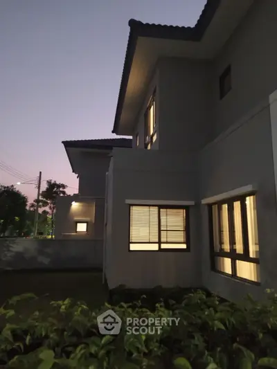 Elegant modern house exterior at dusk with warm interior lighting and lush garden.