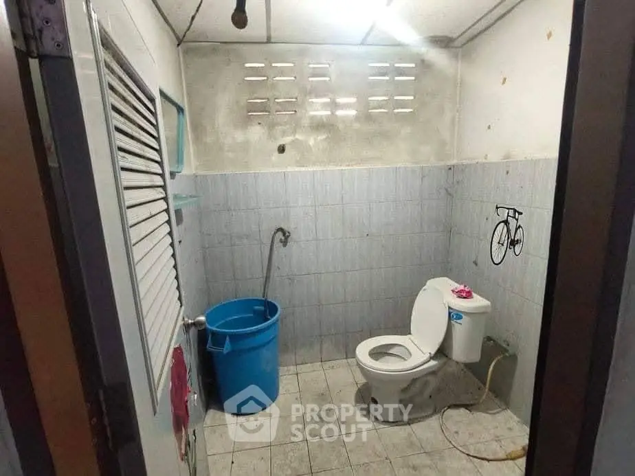 Basic bathroom with toilet and blue bucket in a modest setting.