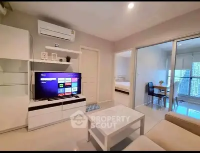 Modern living room with sleek furniture and smart TV, open view to dining area and bedroom.