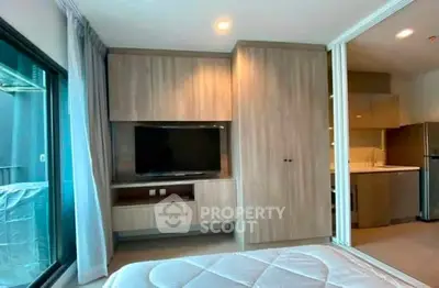 Modern bedroom with built-in TV and sliding doors to kitchen in stylish apartment.