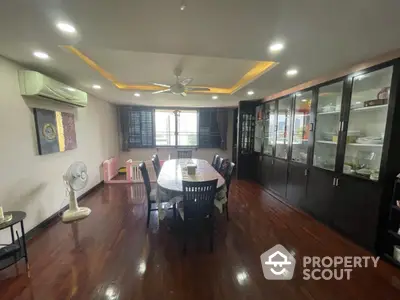 Spacious dining area with polished wooden floors, large dining table, and ample cabinetry, complemented by natural light and modern ceiling fan.