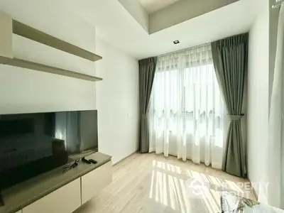 Modern living room with natural light, sleek TV setup, and elegant curtains.