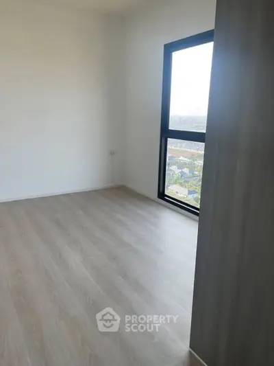 Bright empty room with large window and wooden flooring, perfect for customization.