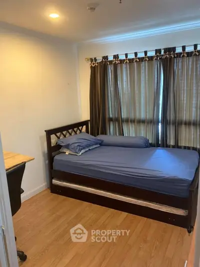 Cozy bedroom with wooden flooring and large window with curtains, featuring a comfortable bed and desk.