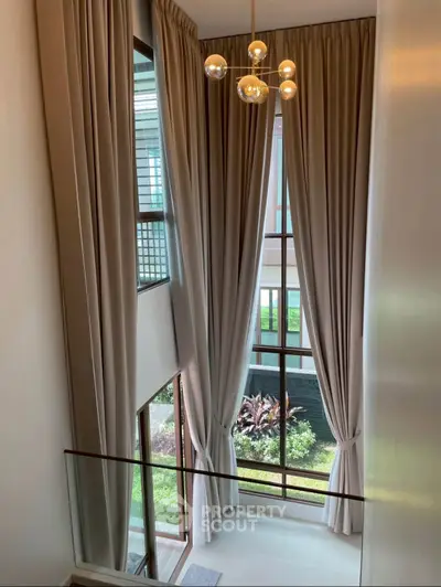 Elegant high-ceiling living room with floor-to-ceiling windows and luxurious drapes