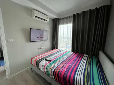 Modern bedroom with striped bedding, wall-mounted TV, and city view through large window.