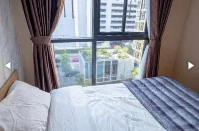 Cozy bedroom with city view through large window, featuring elegant curtains and plush bedding.