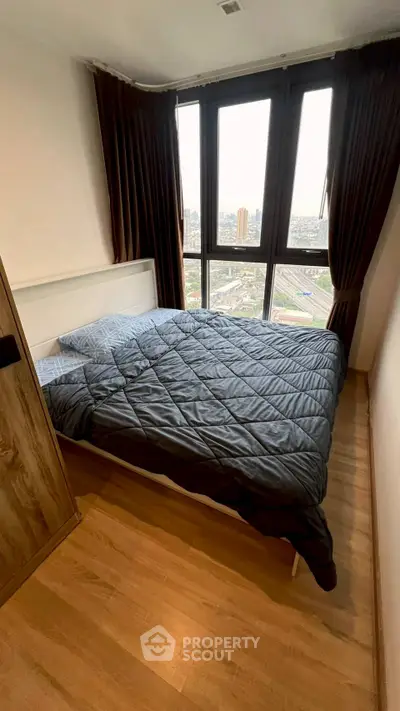 Cozy bedroom with large window offering stunning city views, featuring a comfortable bed and wooden flooring.