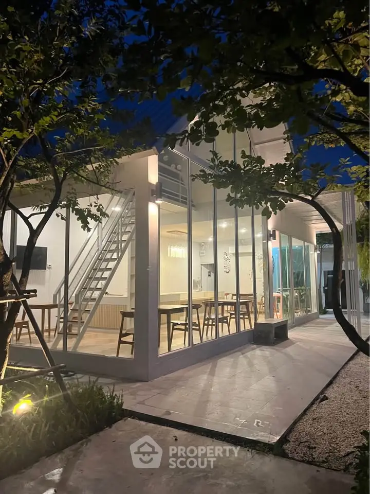 Modern glass-walled building with stylish interior and lush garden setting at dusk.