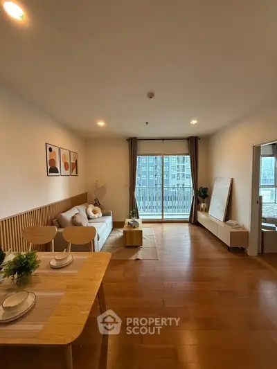 Spacious modern living room with wooden flooring and balcony view in urban apartment.