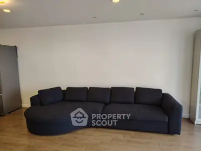 Spacious living room with modern dark sofa and wooden flooring, perfect for relaxation and entertaining.