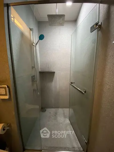 Modern shower with glass doors and rainfall showerhead in sleek bathroom.