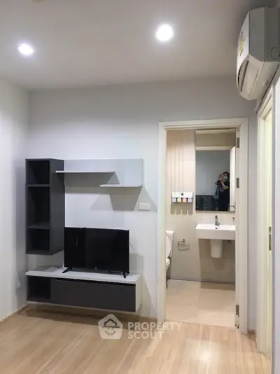 Modern living room with sleek TV unit and view into a compact bathroom.
