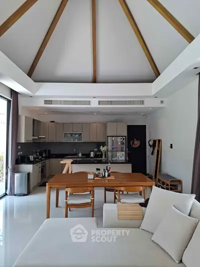 Spacious modern living room with open kitchen and vaulted ceiling, featuring elegant wooden furniture.