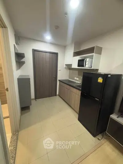 Modern kitchen with sleek cabinetry, black fridge, and microwave in compact apartment.