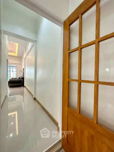 Bright hallway leading to a cozy living room with modern decor and sleek flooring.