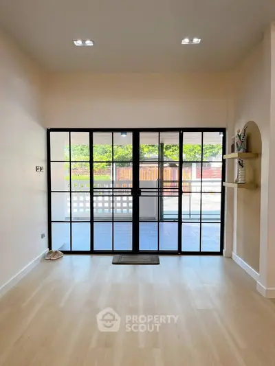Spacious living room with elegant glass doors leading to a patio, featuring light wood flooring and modern decor.