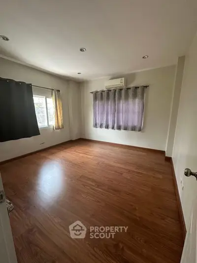 Spacious empty room with wooden flooring and air conditioning, ideal for customization.