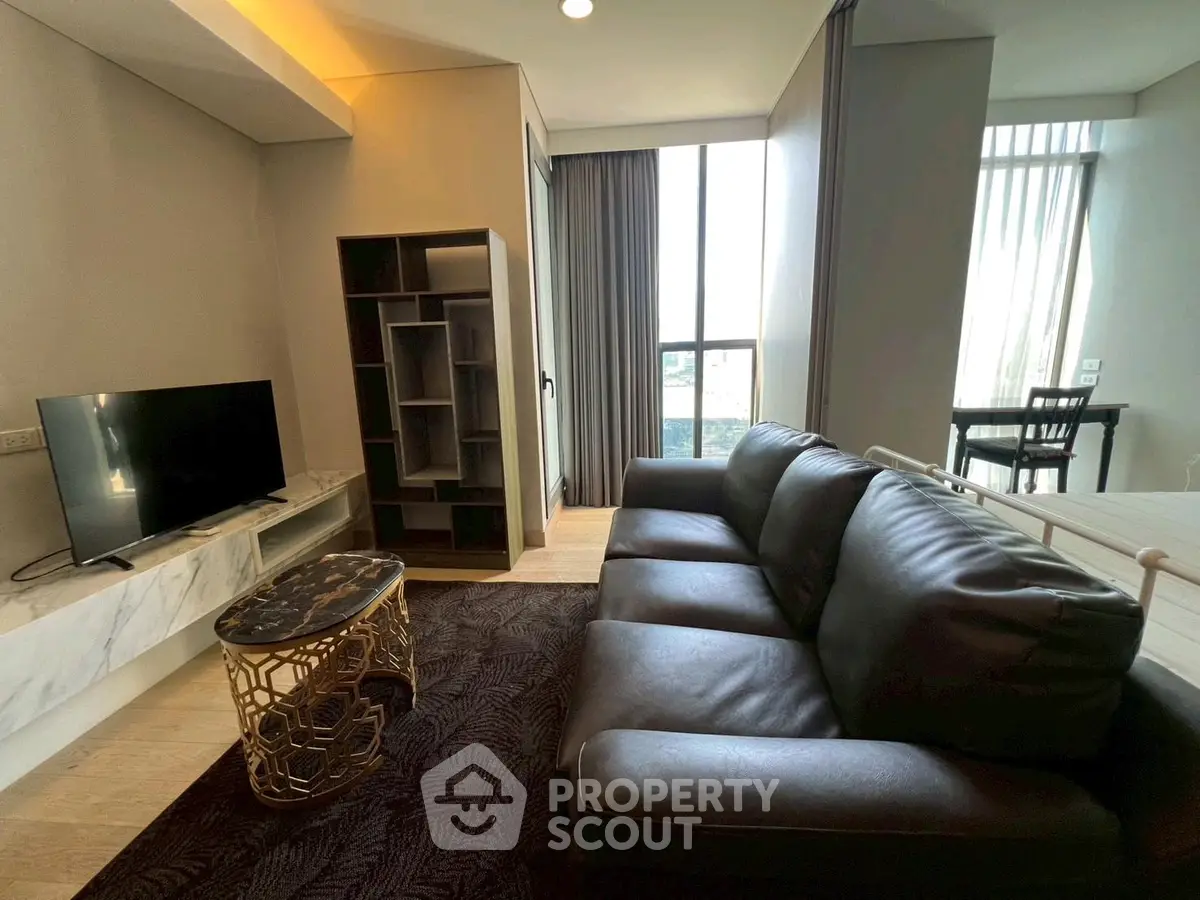 Modern living room with leather sofa and TV, featuring floor-to-ceiling windows and stylish decor.