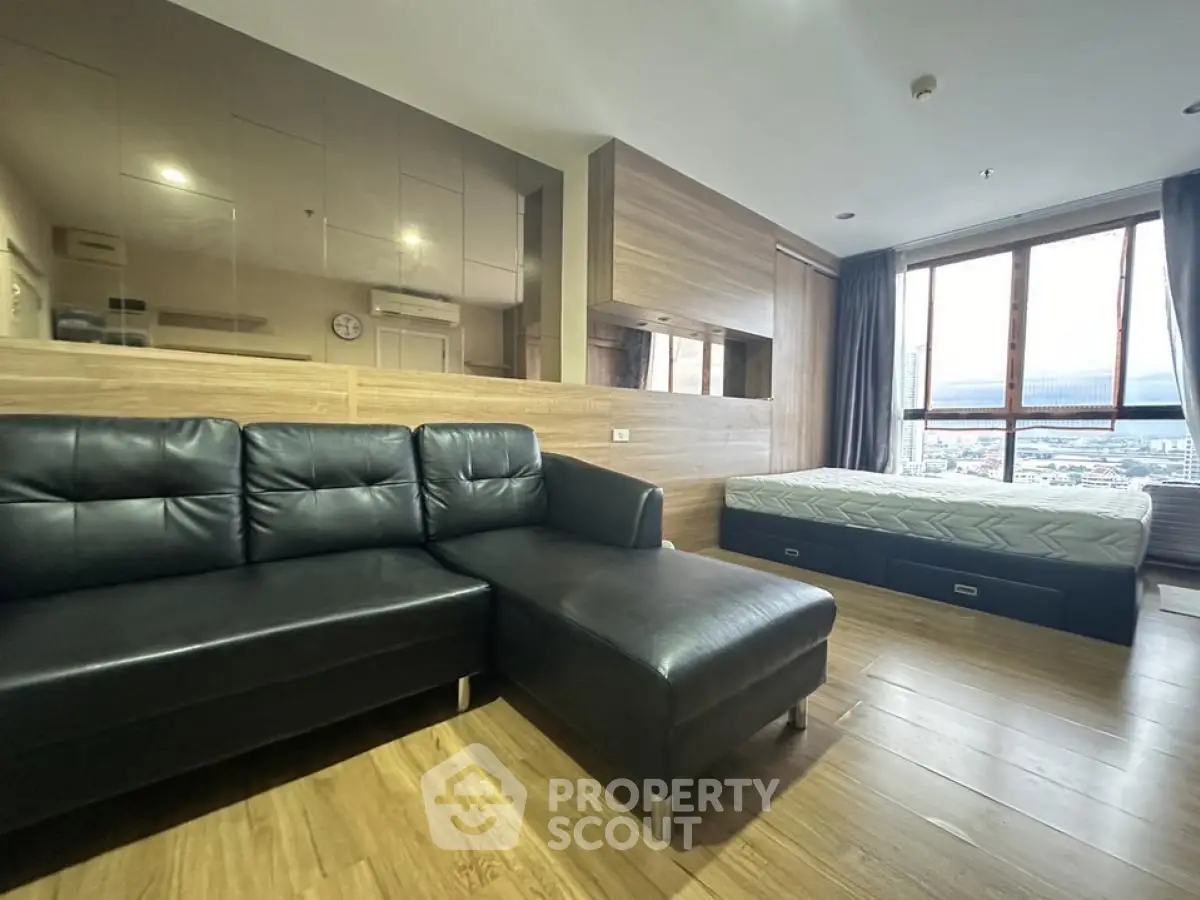 Modern studio apartment with wooden flooring and large windows offering city views.